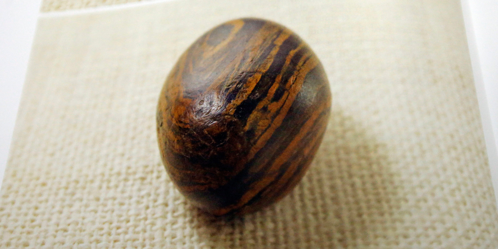 A small stone sits on a cloth. The stone has various small pits and is a dark brown, colored with rust-colored stripes.